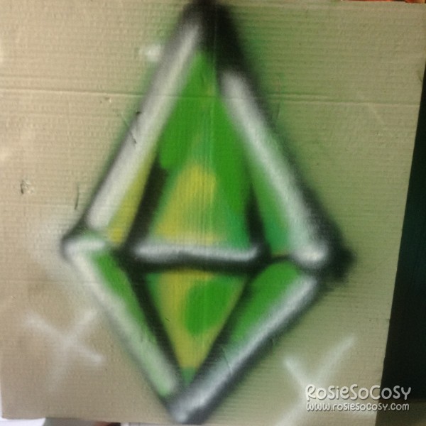 A piece of cardboard with a giant graffiti plumbob on it. It's a green plumbob with black outlines, and white highlights inside.