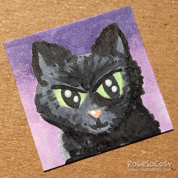An inch sized drawing of a black cat with green eyes. The background is a purple and lilac gradient.