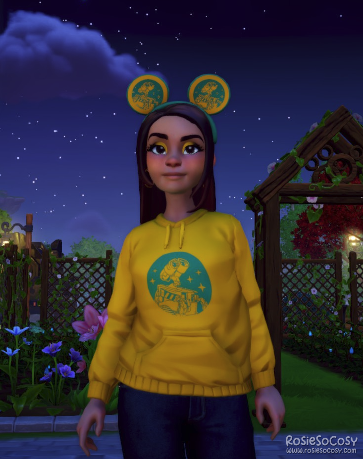 Rosie's avatar in Dreamlight Dreamlight Valley is wearing a yellow hoodie with a teal print of Wall-E, and she has matching Mickey Mouse ears with a yellow/teal Wall-E pattern on them.