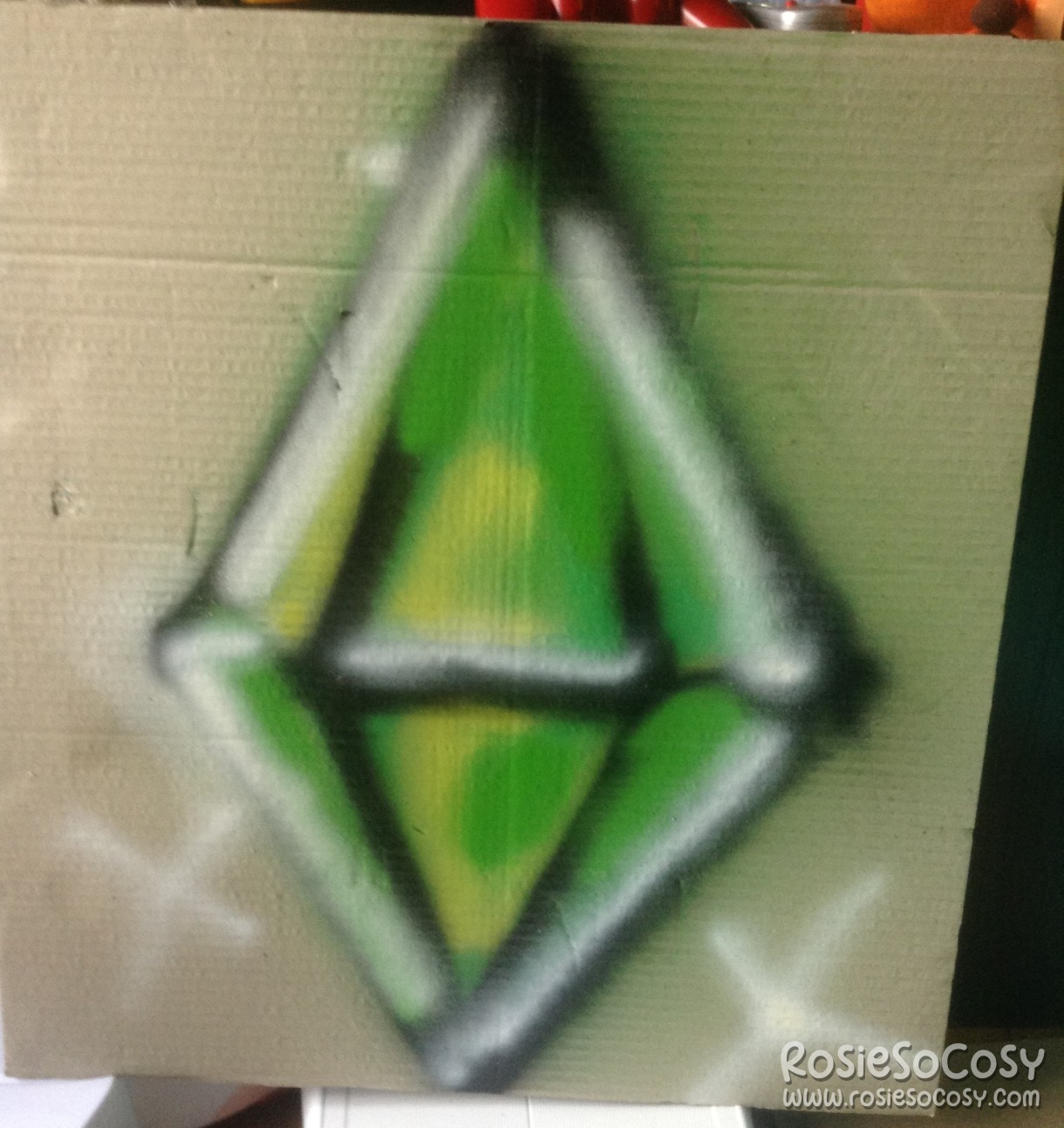 A piece of cardboard with a giant graffiti plumbob on it. It's a green plumbob with black outlines, and white highlights inside.