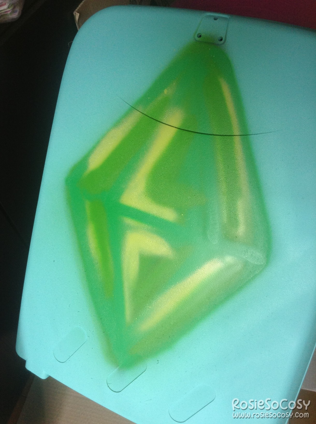 Part of a suitcase. The suitcase is a soft aqua colour. There's a big green graffiti plumbob on it.
