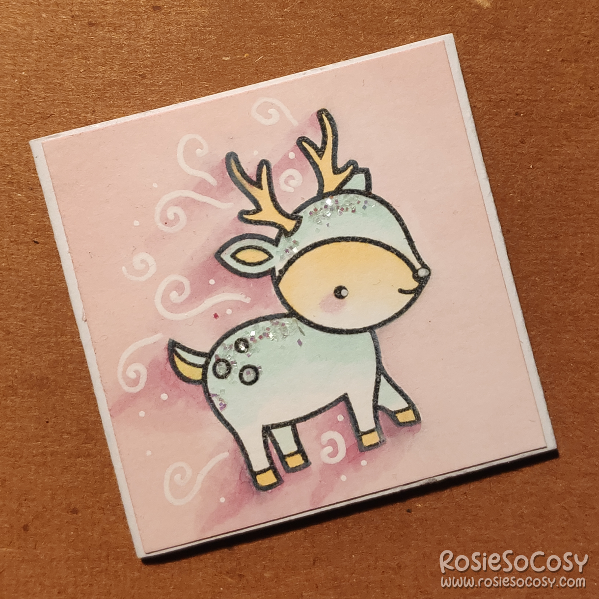 An inch sized card with a light pink background, and a light blue deer which seems to be rushing or running towards (or from) something.